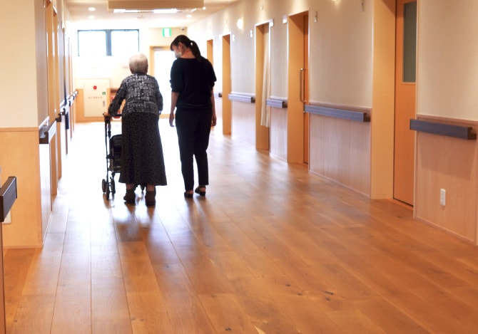 介護・福祉施設内を歩く高齢者と施設関係者